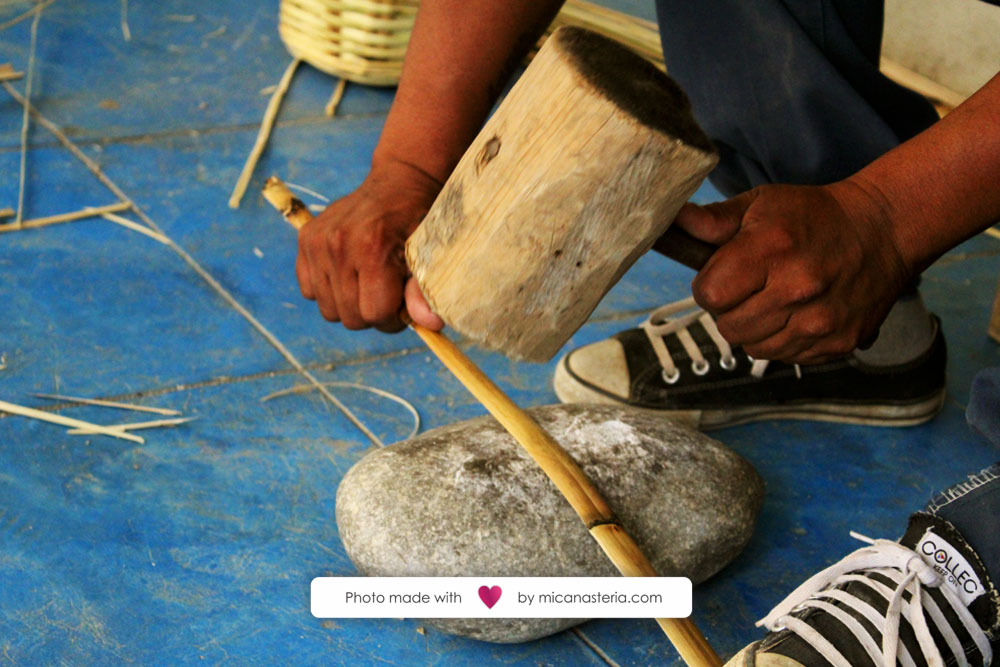 Artesano golpeando con un mazo de madera una tira de carrizo.